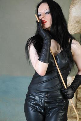 15P Dark haired mistress wields a cane while attired in leather clothes and gloves