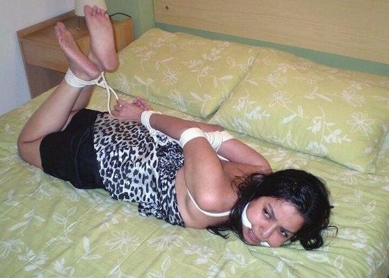 16P Dark-haired girl is cleave gagged and hogtied on a bed in a dress