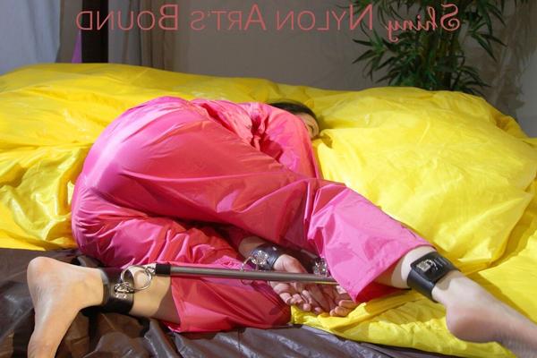 16P ルーシーはセクシーなピンクの光沢のあるナイロンの雨を着てベッドの上でバーで縛られて猿ぐつわをされています