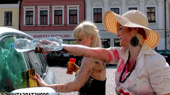 14P Closed women cover each other in food products between parked cars