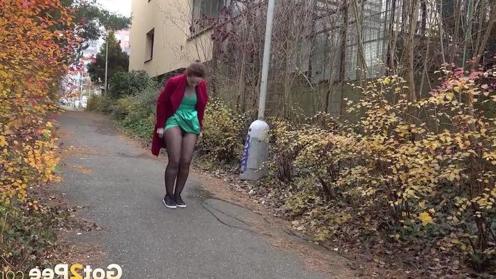 15P Caucasian female Lora takes a piss while walking on a pathway in the city