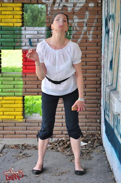 15P Fully clothed brunette Mina smokes a cigarette in front of a brick wall