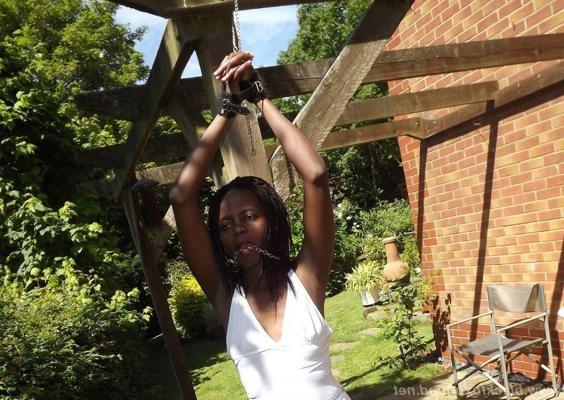 16P Black girl is cleaved gagged and bound with her hands above her head in a yard