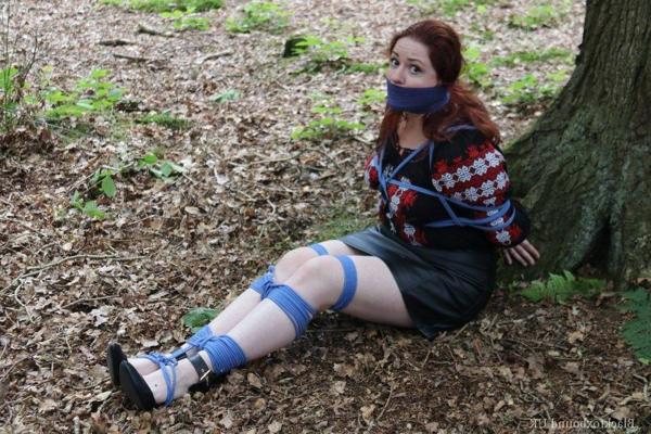16P Pale redhead is silenced with a gag while tied up in her clothes under a tree
