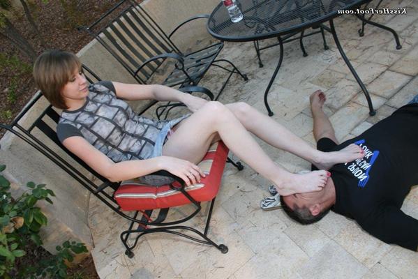 12P Caucasian woman Mistress Kylie rubs her bare feet over a man's face on a patio
