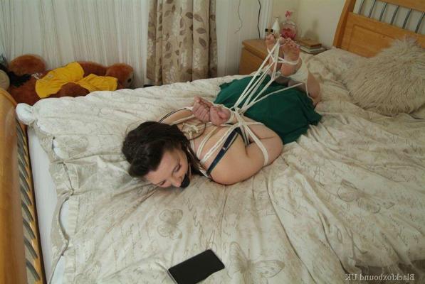16P Brunette chick is left face down on a bed while hogtied and ball gagged