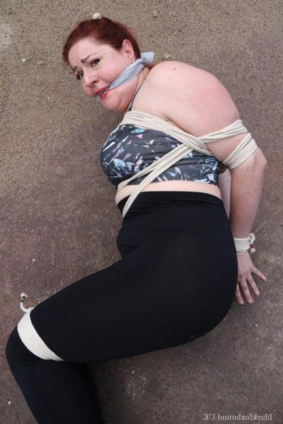 16P Redheaded girl Mada Rose is left on a paved lot while tied up