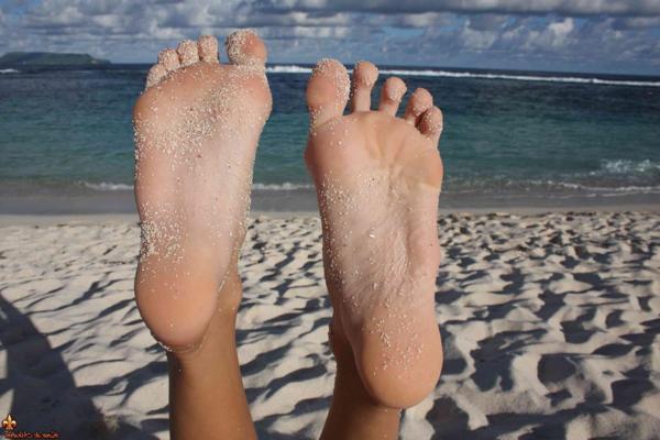 12P Caucasian girl shows the bottoms of her sand covered feet on a beach