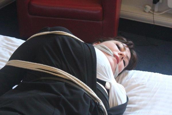 16P Dark haired lady shows her brassiere while bound and gagged on a bed